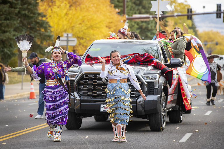 Native American students wearing jingle dress regalia walking in a parade