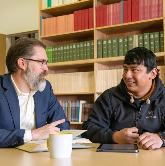 Professor and student talking in front of bookcase