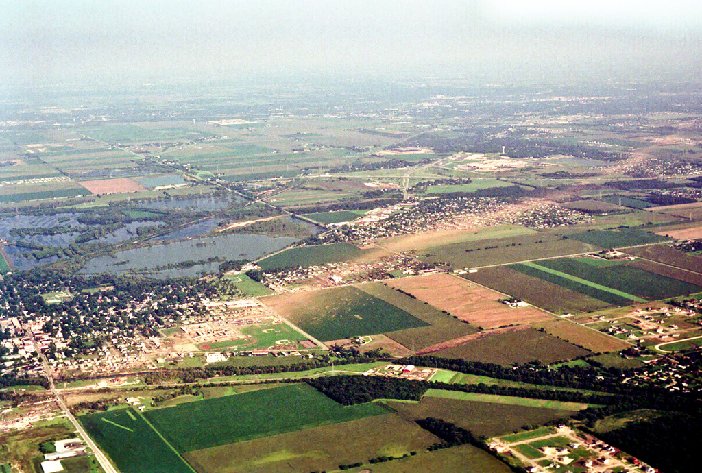 Photo showing damage path of 1990 Plainfield tornado from an airplane. Damage to buildings and vegetation is evident, which creates a clear path from near the foreground to the background. Photo vantage is from just west of Plainfield looking east-southeastward.