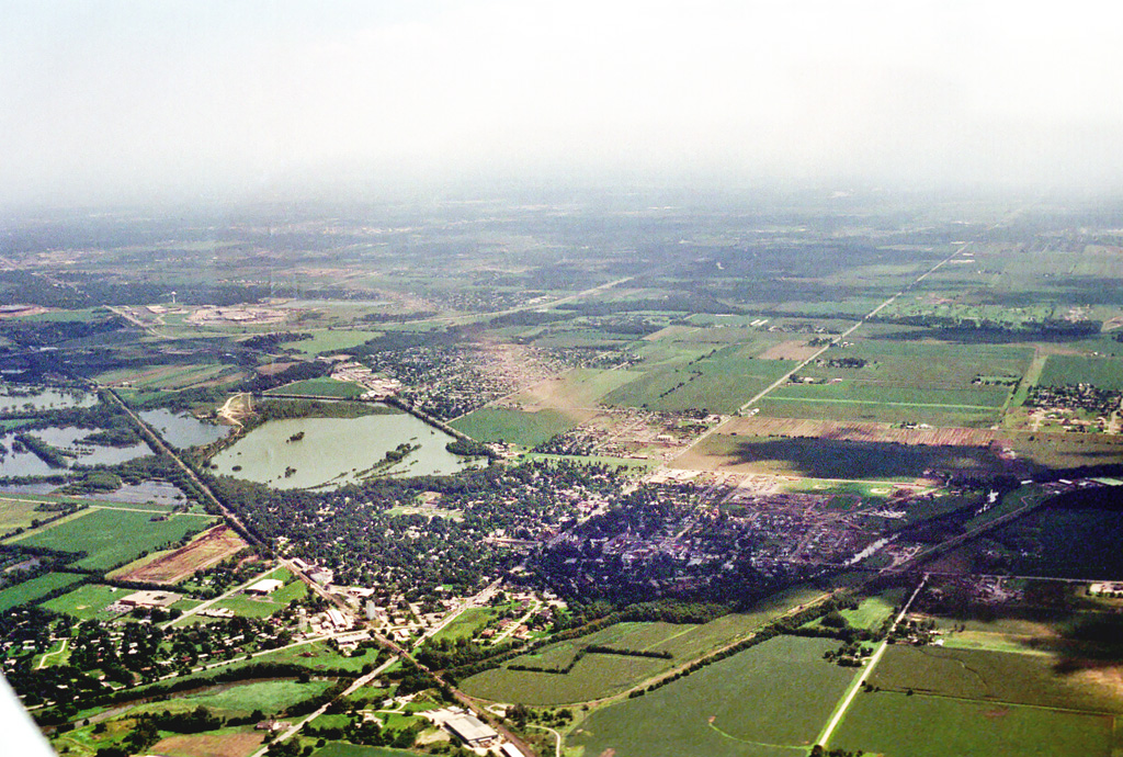 Photo showing damage path of 1990 Plainfield tornado from an airplane. Damage to buildings and vegetation is evident, which creates a clear path from near the foreground to the background. Photo vantage is from just northwest of Plainfield looking south-southeastward