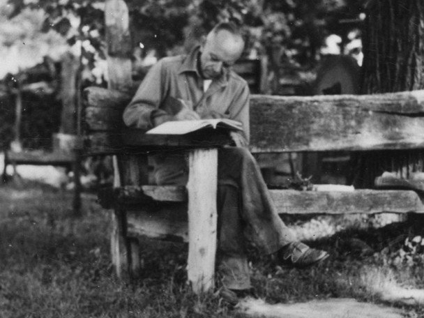 Aldo Leopold sitting on a bench, outdoors, writing.