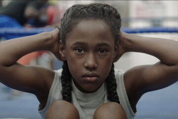 A Black girl covers her ears while staring into the camera