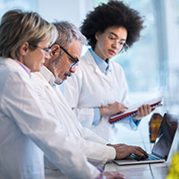 Three scientists working in a laboratory. Focus is on mature man typing on laptop